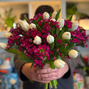 Η ανθοδέσμη με λευκές τουλίπες και γαλλικό γαρύφαλλο είναι ένας ύμνος στην απλότητα και την αρμονία των αντιθέσεων. Το αγνό λευκό των τουλιπών συναντά το έντονο ροζ–φούξ των γαλλικών γαρύφαλλων, δημιουργώντας μια σύνθεση που συνδυάζει την καθαρότητα με τη ζωντάνια. Η έμπνευση αντλείται από την εναλλαγή του χειμώνα και της άνοιξης, όταν το φως συναντά το χρώμα και η φύση ξαναγεννιέται.