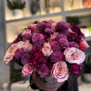 Στο επίκεντρο της σύνθεσης βρίσκονται τα ροζ ολλανδικά τριαντάφυλλα, γνωστά για τη φινέτσα και την πλούσια άνθισή τους. Με τα μεγάλα, μεταξένια πέταλα και τις απαλές διαβαθμίσεις του χρώματος, φέρνουν στο μπουκέτο μια αίσθηση πολυτέλειας και ρομαντικής νοσταλγίας. Δίπλα τους, τα χρυσάνθεμα σαντίνι προσθέτουν ένταση και δομή, με τα μικρά, σφαιρικά τους άνθη να δημιουργούν όμορφη υφή και οπτικό ενδιαφέρον. Ο συνδυασμός αυτός ολοκληρώνεται με το γαλλικό γαρύφαλλο, ένα άνθος με διαχρονική αξία στην ανθοδετική, που ενισχύει τον όγκο και το χρώμα, προσδίδοντας έναν τόνο κλασικής κομψότητας. Κάθε λουλούδι παίζει τον ρόλο του στη σύνθεση, δημιουργώντας ένα αποτέλεσμα αρμονικό και γεμάτο ζωή.