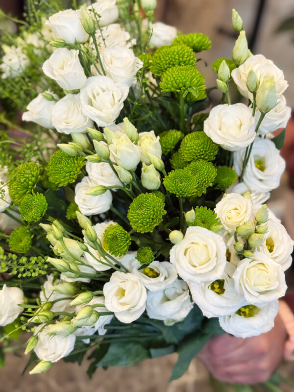 Κεντρικό ρόλο στη σύνθεση κατέχουν οι λυσίανθοι, λουλούδια που ξεχωρίζουν για τη λεπτότητα και την αέρινη υφή τους. Με τα απαλά λευκά πέταλα και τα πράσινα μπουμπούκια τους, αποπνέουν ρομαντισμό, αγνότητα και διακριτική φινέτσα.