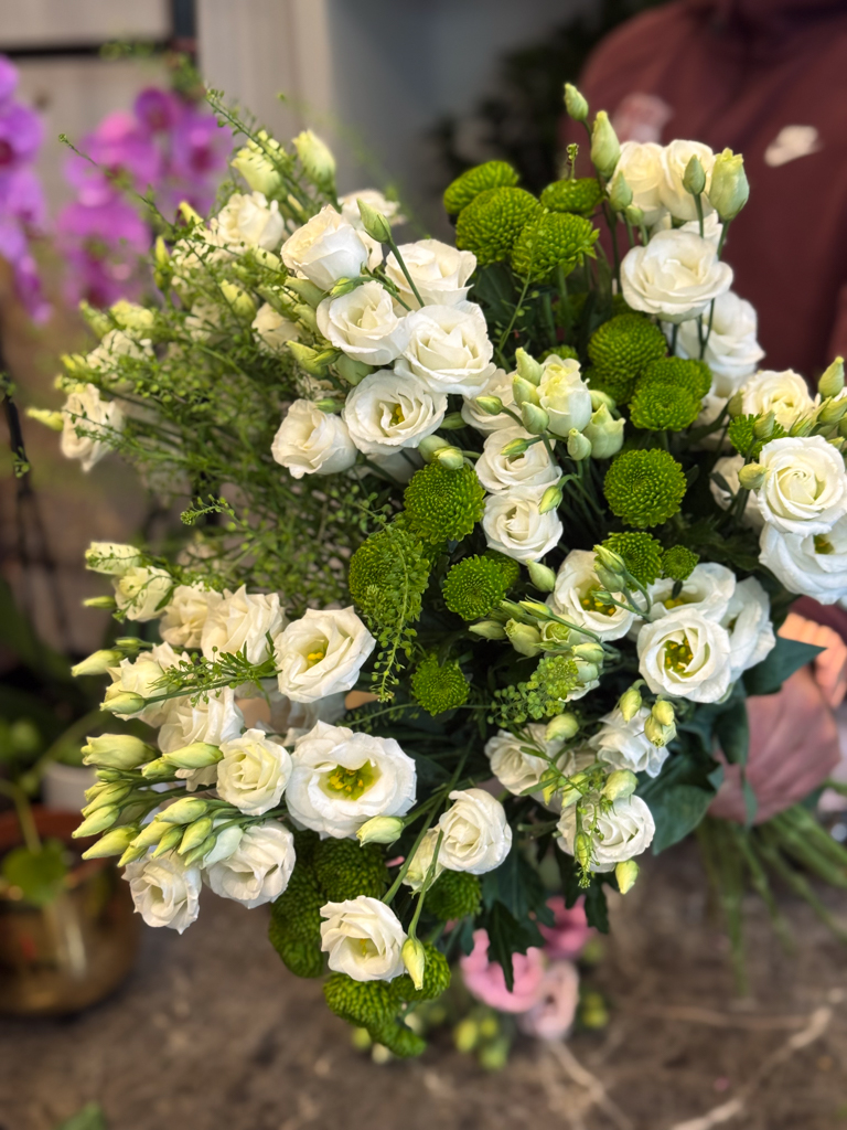 Κεντρικό ρόλο στη σύνθεση κατέχουν οι λυσίανθοι, λουλούδια που ξεχωρίζουν για τη λεπτότητα και την αέρινη υφή τους. Με τα απαλά λευκά πέταλα και τα πράσινα μπουμπούκια τους, αποπνέουν ρομαντισμό, αγνότητα και διακριτική φινέτσα.