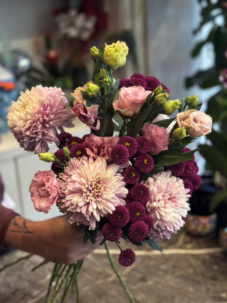 Στην ίδια σύνθεση, οι λυσιάνθοι προσθέτουν ένα πιο ρομαντικό και αέρινο στοιχείο. Πρόκειται για άνθη με λεπτά, μεταξένια πέταλα και πράσινα μπουμπούκια που σταδιακά ανοίγουν, συμβολίζοντας την αναγέννηση και τη φρεσκάδα.