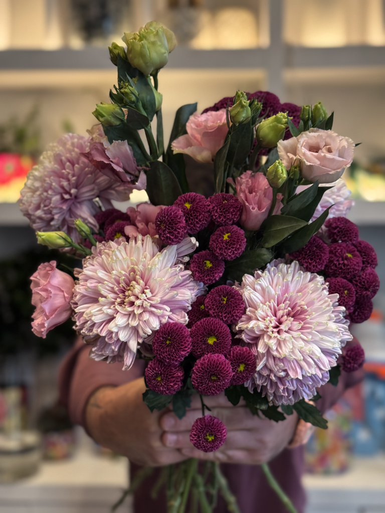 Στην ίδια σύνθεση, οι λυσιάνθοι προσθέτουν ένα πιο ρομαντικό και αέρινο στοιχείο. Πρόκειται για άνθη με λεπτά, μεταξένια πέταλα και πράσινα μπουμπούκια που σταδιακά ανοίγουν, συμβολίζοντας την αναγέννηση και τη φρεσκάδα.