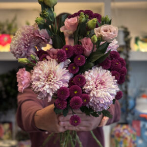 Τα σαντίνι χρυσάνθεμα — γνωστά για το στρογγυλό, μικρό τους άνθος — προσδίδουν όγκο και ένταση στη σύνθεση. Με το βαθύ, πλούσιο μωβ τους, δημιουργούν ένα δυνατό οπτικό σημείο, αναδεικνύοντας τα υπόλοιπα άνθη γύρω τους.