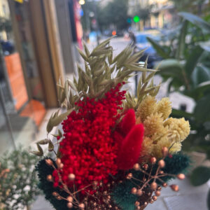 Η σύνθεση περιλαμβάνει αποξηραμένα στάχυα, amaranthus σε έντονο κόκκινο, bunny tails σε βαθύ κεραμιδί, χρυσαφένια άνθη και διακοσμητικά με μεταλλικές μπρονζέ πινελιές. Ο συνδυασμός των υφών δημιουργεί πλούσιο όγκο και γιορτινή διάθεση, χωρίς να απαιτείται καμία φροντίδα.