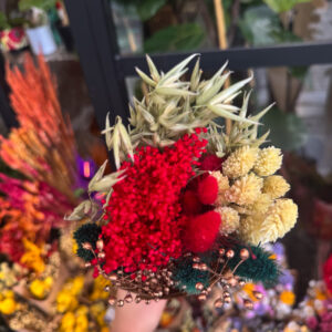 Η σύνθεση περιλαμβάνει αποξηραμένα στάχυα, amaranthus σε έντονο κόκκινο, bunny tails σε βαθύ κεραμιδί, χρυσαφένια άνθη και διακοσμητικά με μεταλλικές μπρονζέ πινελιές. Ο συνδυασμός των υφών δημιουργεί πλούσιο όγκο και γιορτινή διάθεση, χωρίς να απαιτείται καμία φροντίδα.